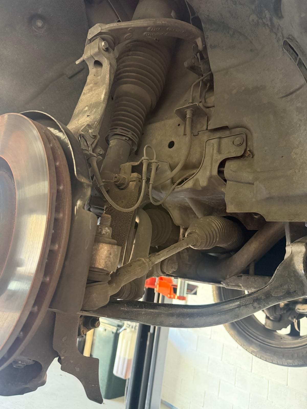 Underside view of a car's front hub showing the brake disc, strut and control arms during brake and suspension work at the North Albury workshop