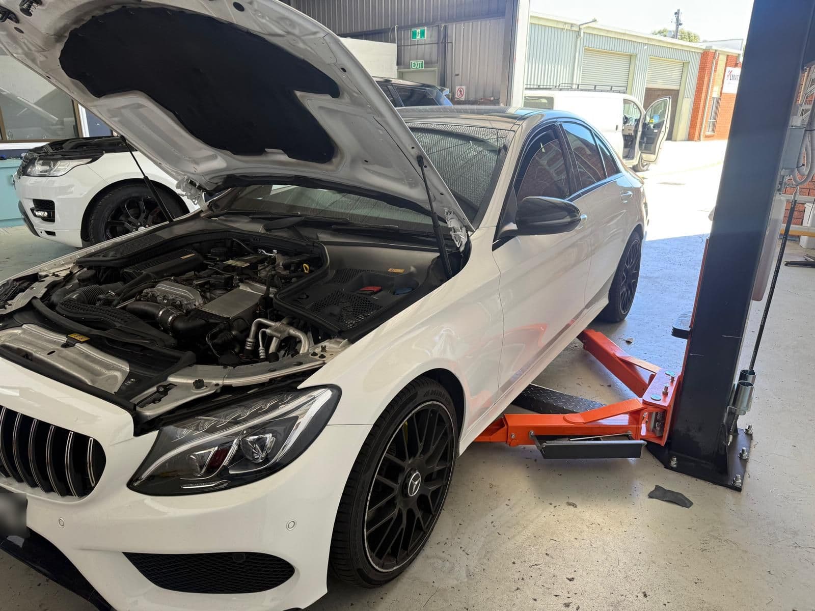 A white Mercedes-Benz sedan on the workshop hoist with the bonnet raised and engine bay open during a logbook service in North Albury